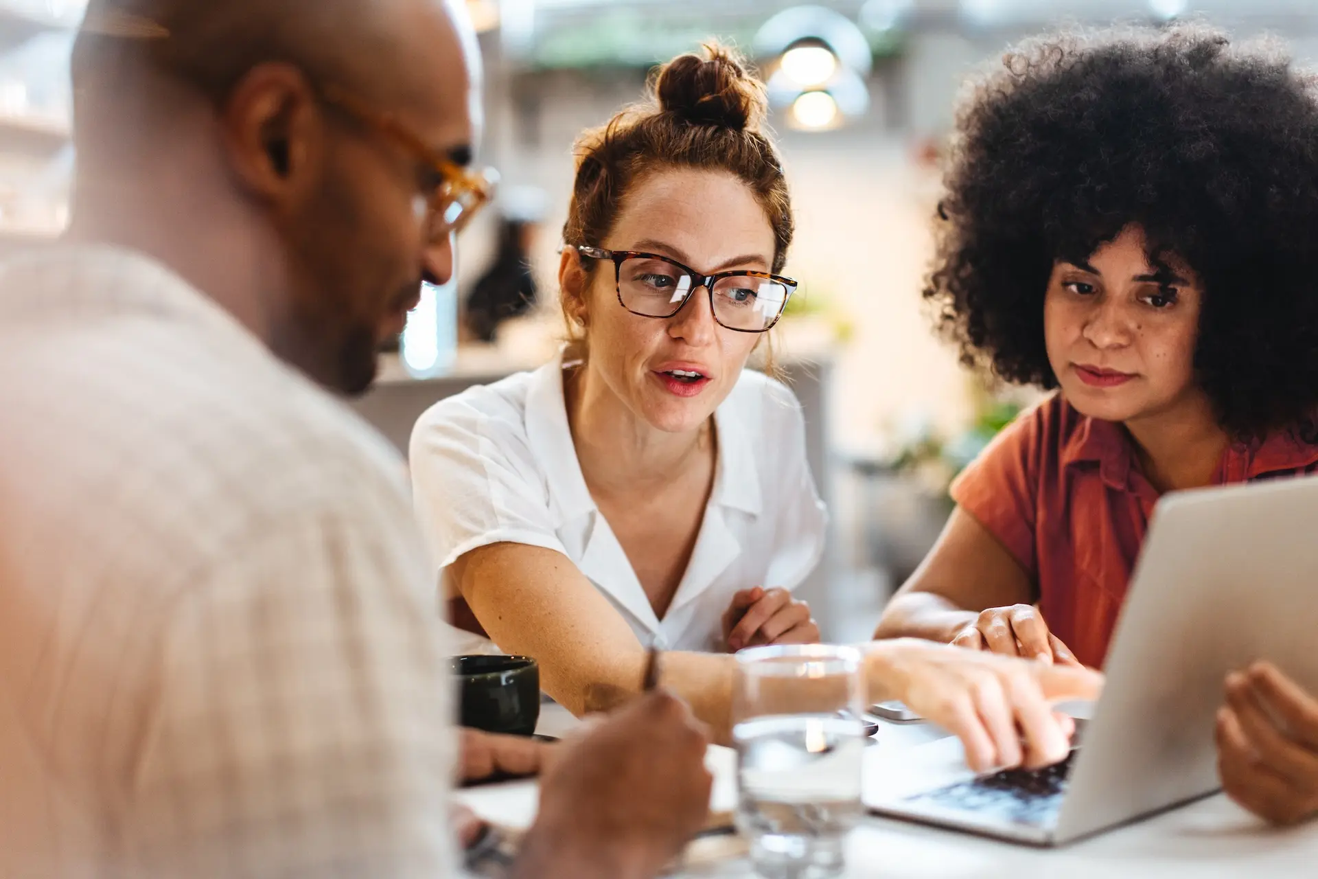 A woman points out something on a computer while another woman looks on, and a man jots notes.